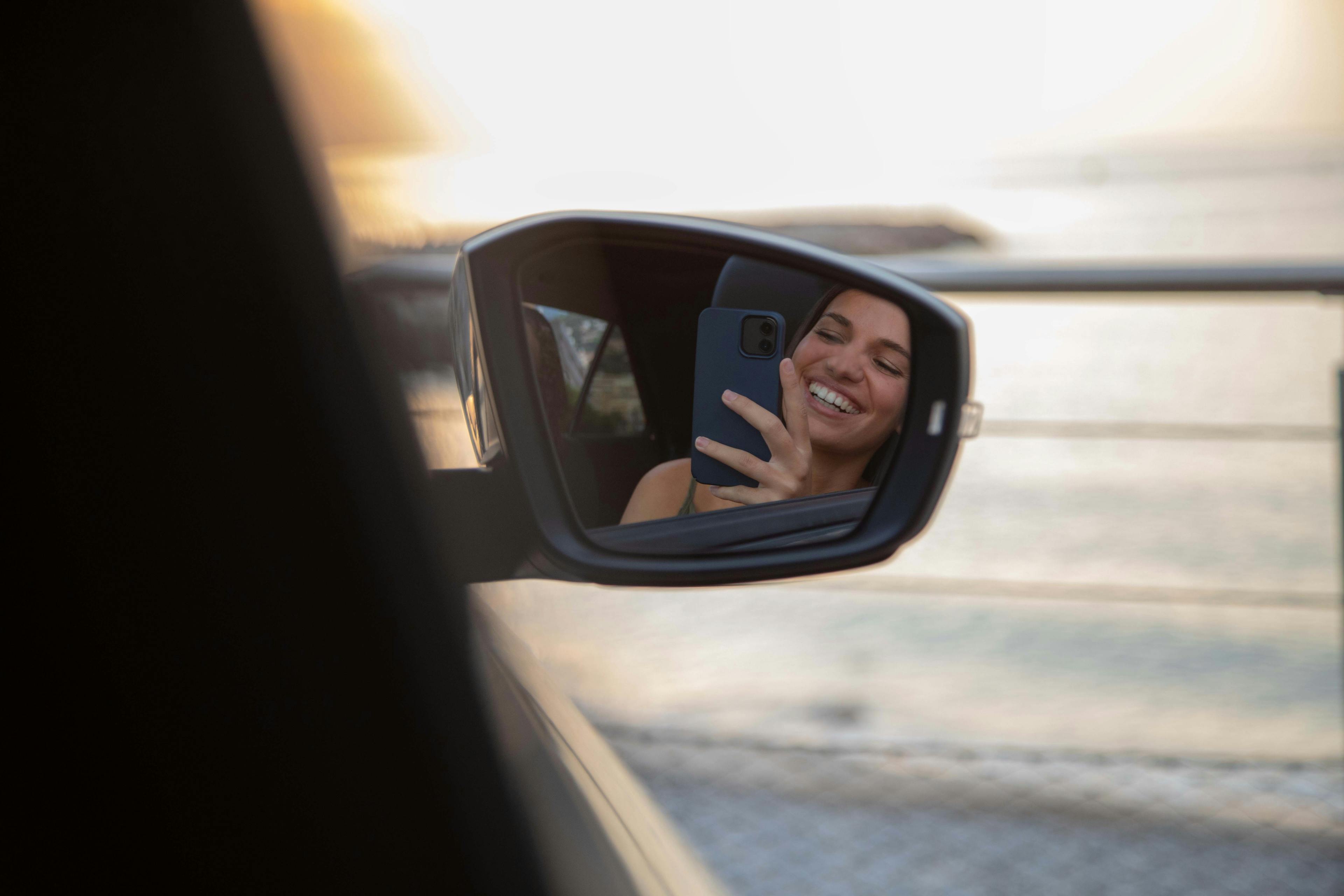 Femme qui se prend en photo avec son téléphone dans le rétroviseur d'une voiture